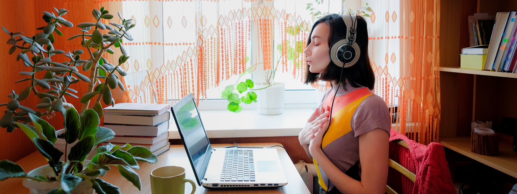 Female in headphones sits at front of laptop and breathing. Online audio meditation concept.